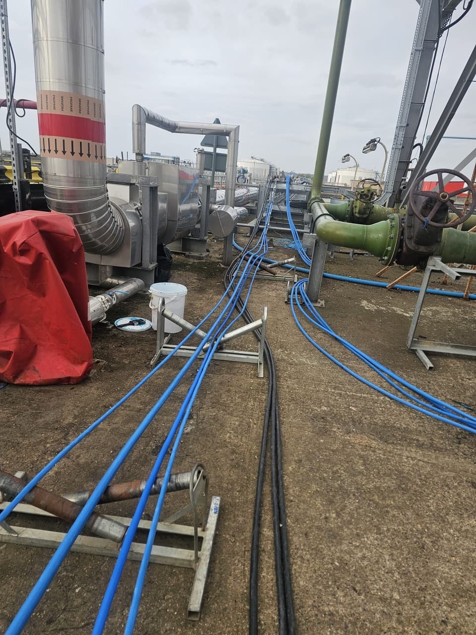 New blue cable runs laid out on rollers between the propane lines and process pipework at the terminal