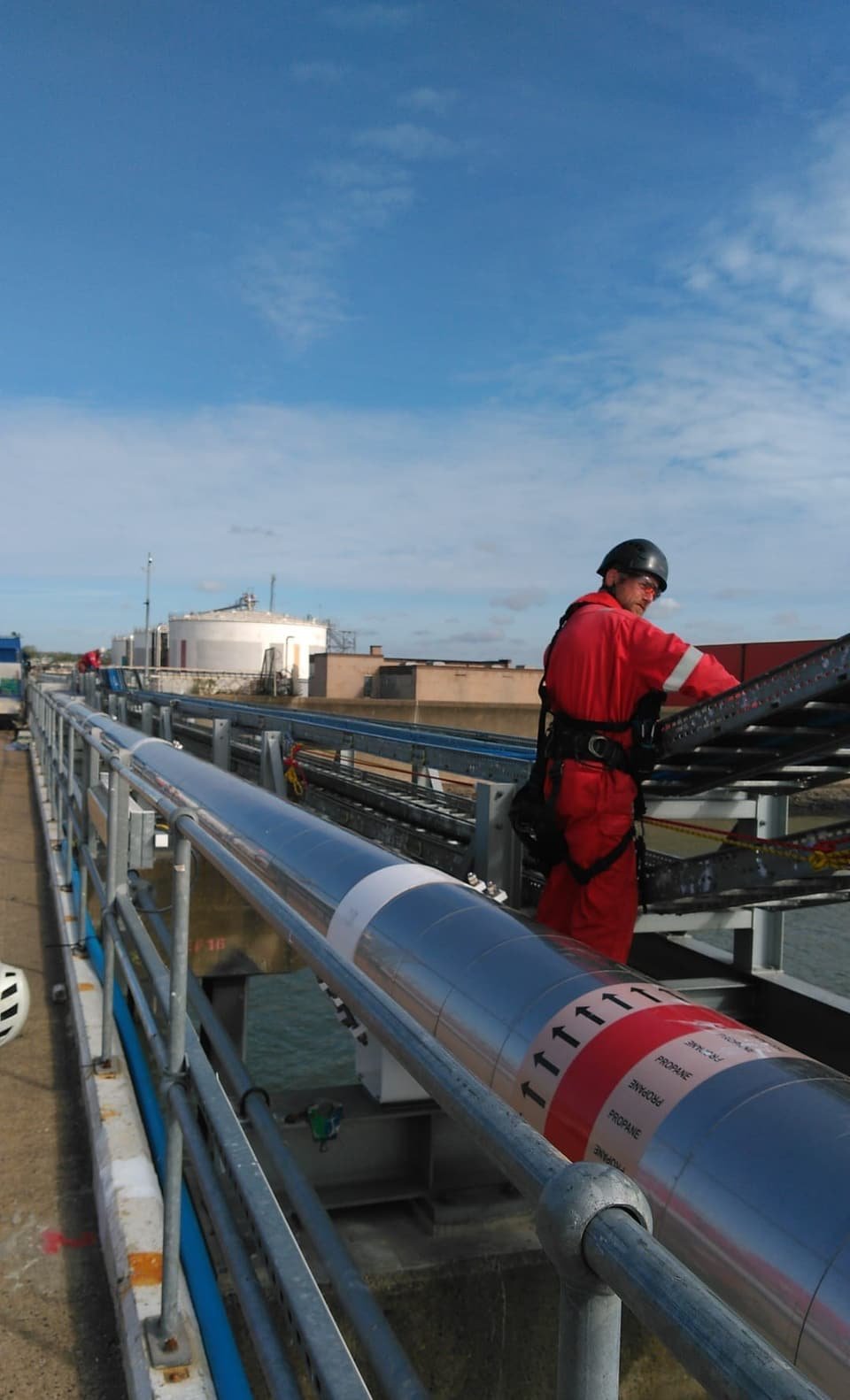 RAT Work technician in flame-resistant coveralls and harness working on a cable tray beside a propane line