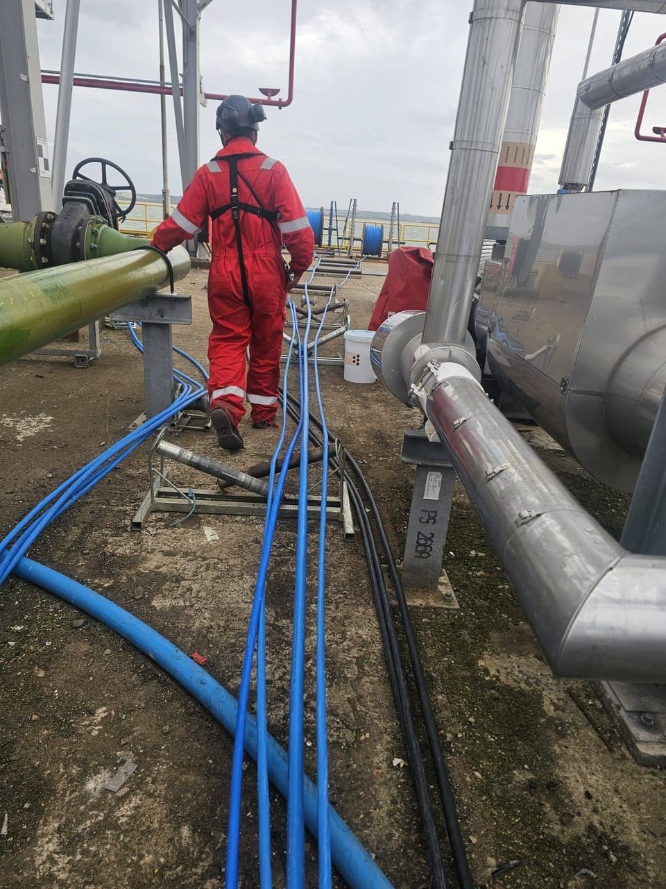 RAT Work technician walking beside new cable runs laid out on rollers between process pipework