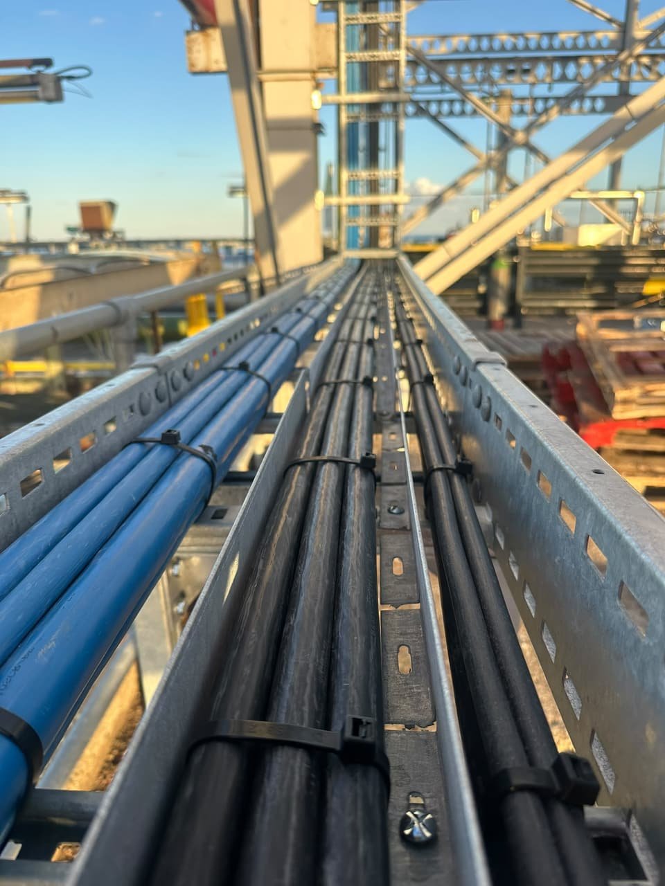 Blue and black cables laid in the tray and secured with cable ties, running along the jetty structure