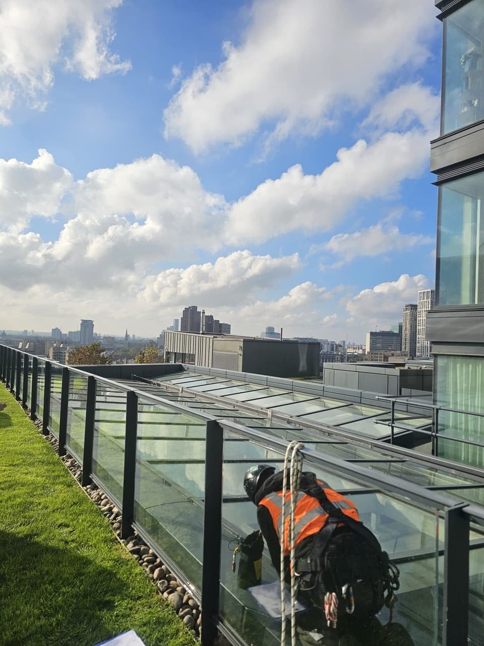 Technician on rope at the edge of rooftop glazing, with the London skyline behind