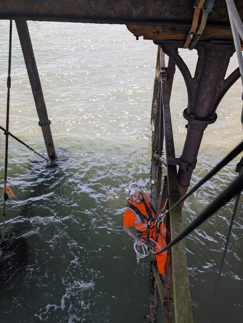RAT Work technician on rope over the sea, working between the iron legs of a pier