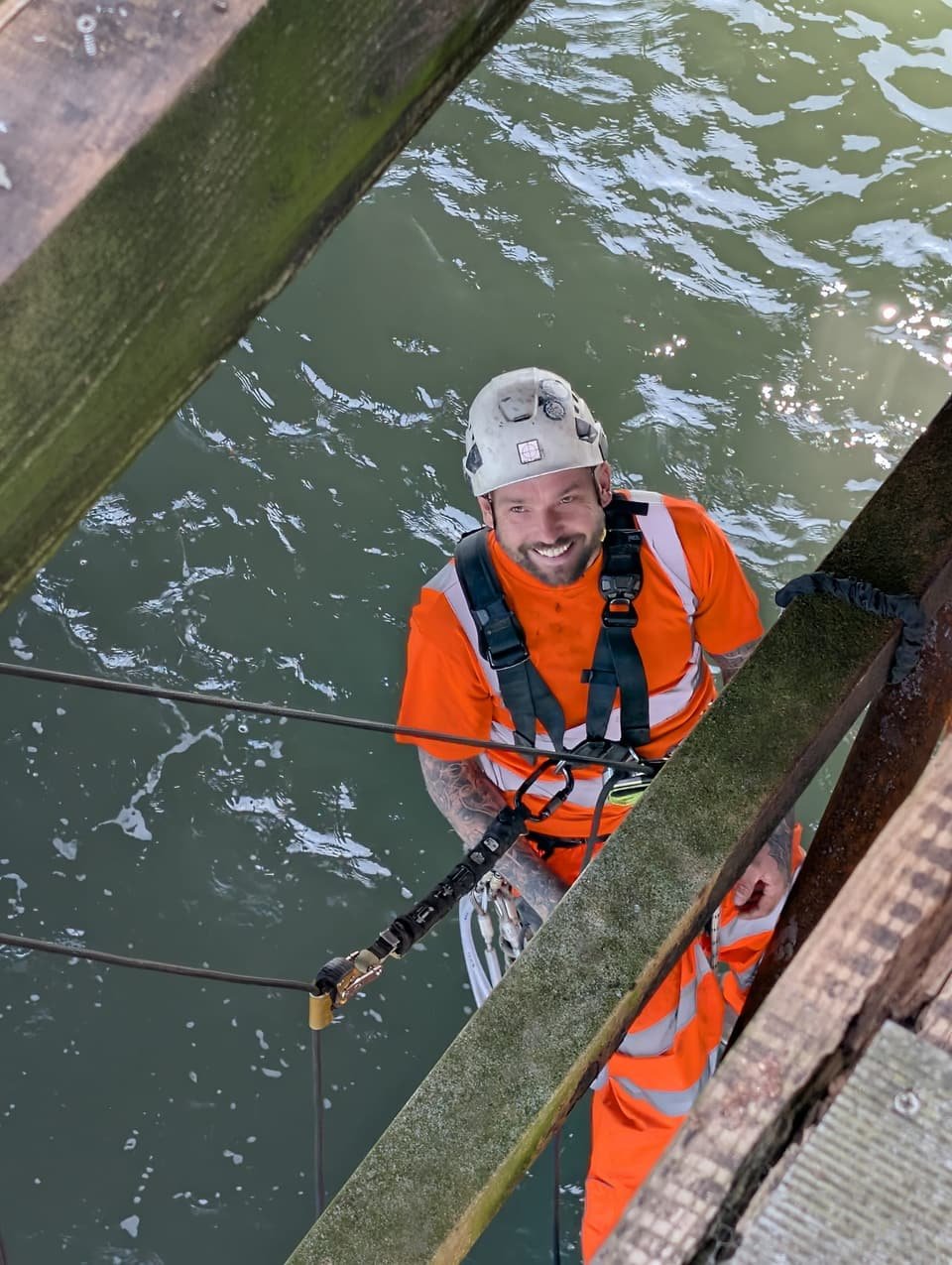 RAT Work technician on rope under a pier, looking up from beside the timber framing