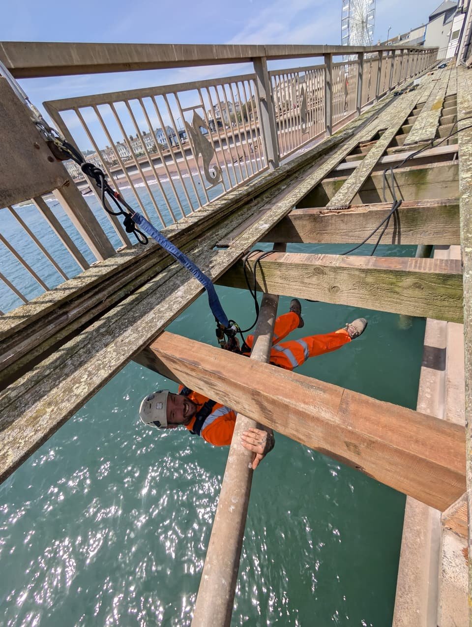 Technician working under the edge of a pier deck, with the promenade and seafront behind