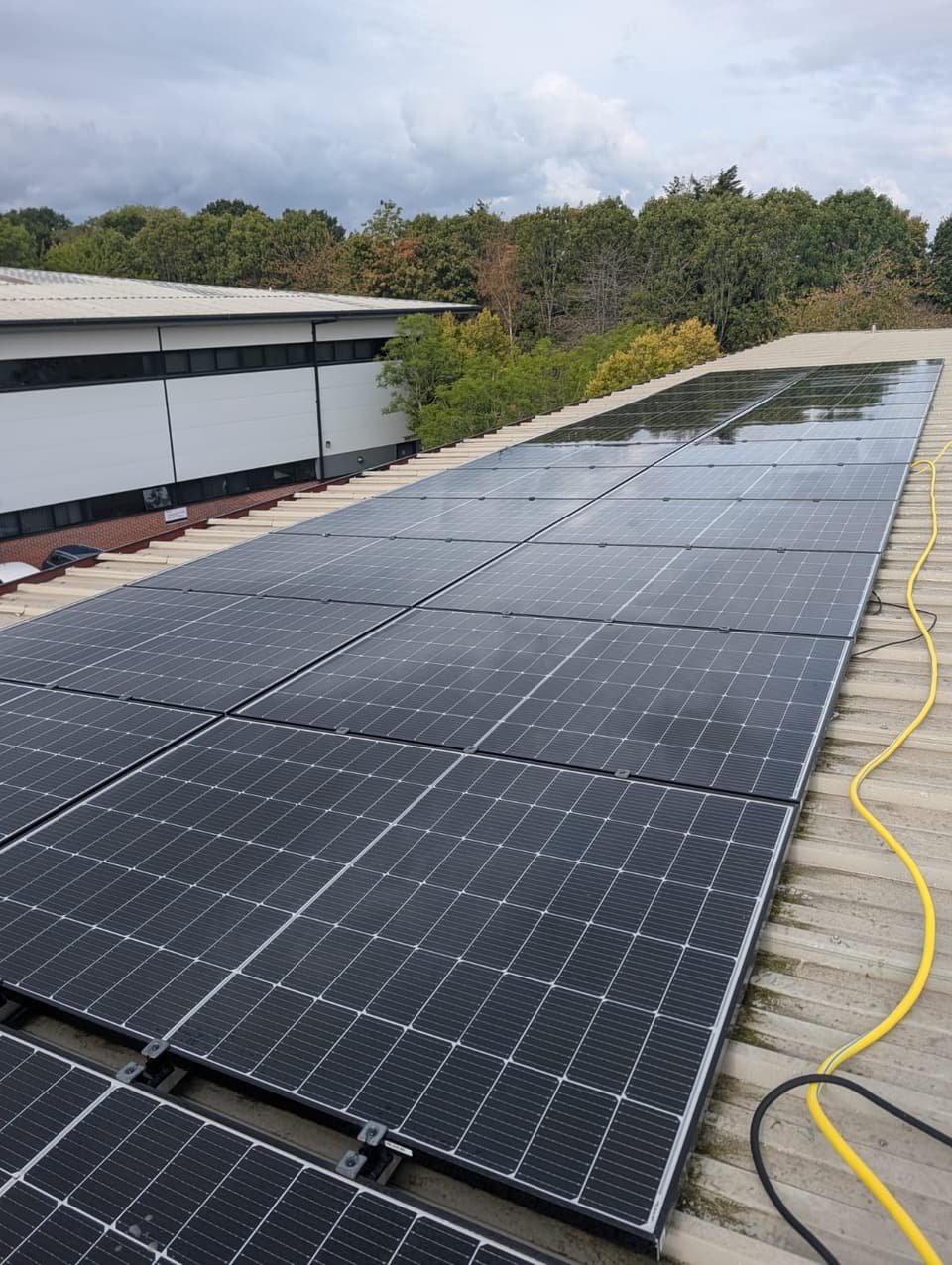 A long rooftop solar array on a warehouse roof, freshly washed with pure water