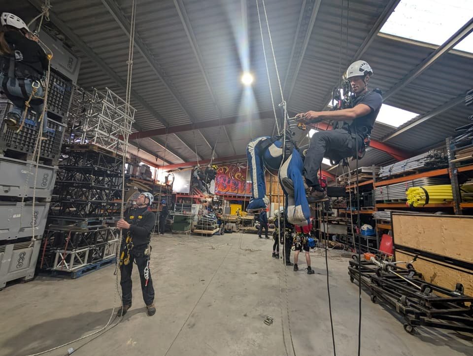 Technique day in a warehouse: a technician on rope practising a pick-off rescue of a casualty dummy while others rig and climb around him